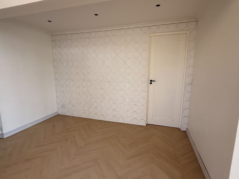 An empty bedroom featuring light wood herringbone flooring, recessed ceiling lighting, and a decorative textured feature wall.