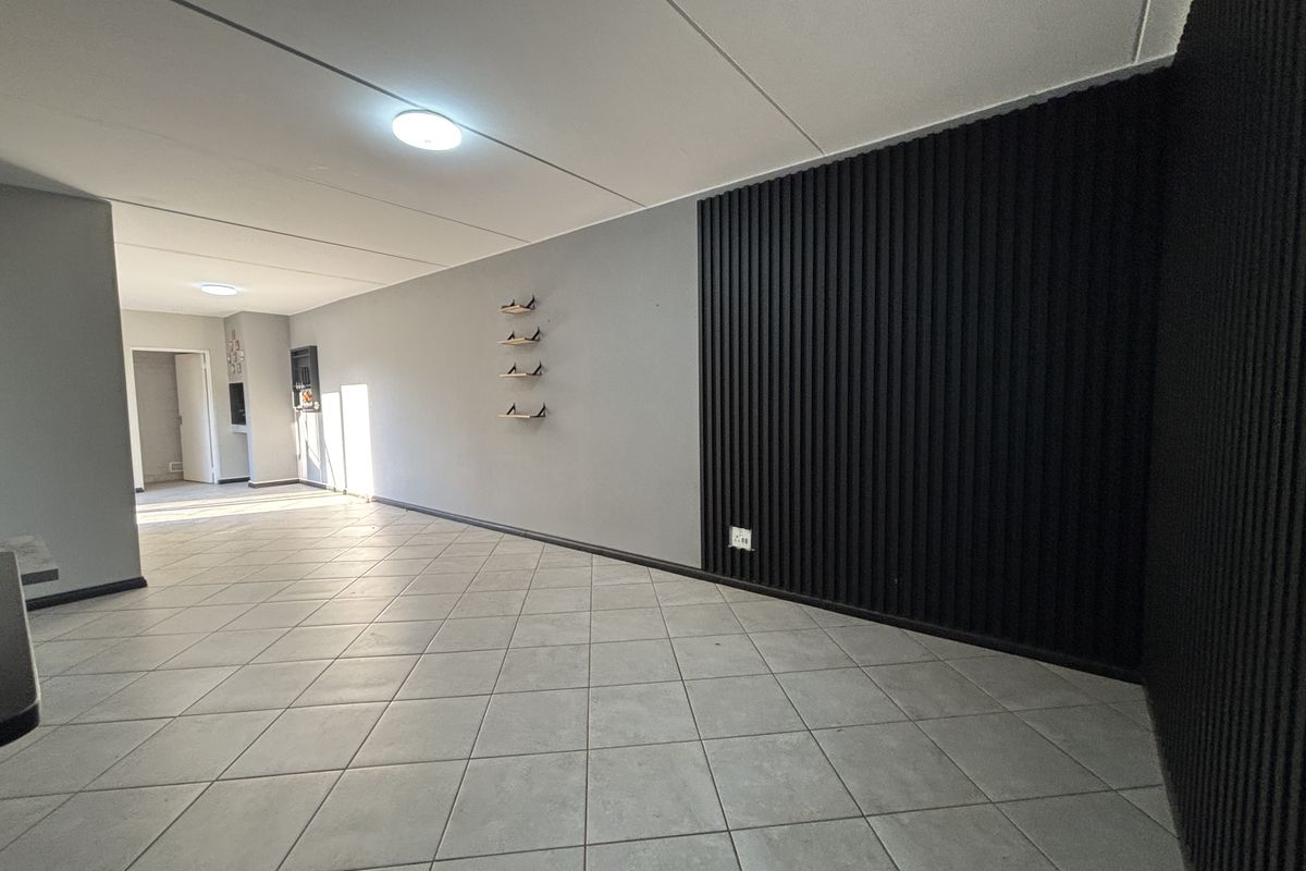 Spacious open-plan living area featuring neutral tiled flooring and a modern black slatted feature wall, offering a clean and contemporary aesthetic.