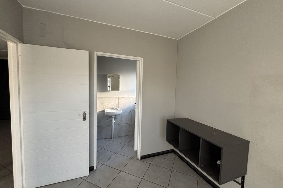 A vacant bedroom featuring tiled flooring, a wall-mounted storage unit, and direct access to an adjoining bathroom area.