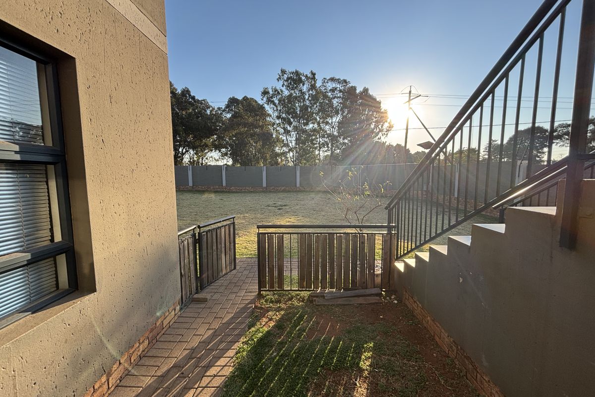 Rear exterior view of the townhouse featuring a paved walkway, metal staircase with balustrade, and a private garden area enclosed by a perimeter wall.