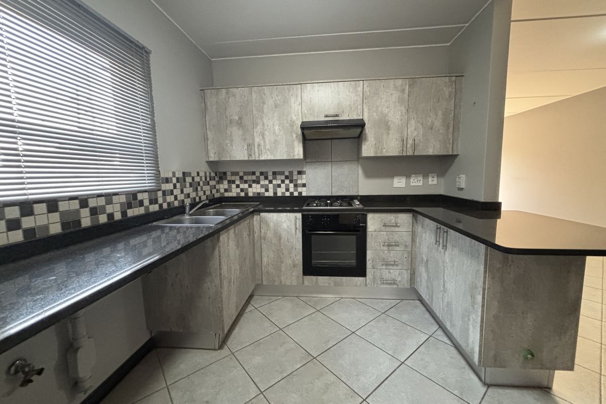 A functional kitchen featuring wood-look cabinetry, granite countertops, built-in oven, gas hob, and tiled flooring with a neutral backsplash.
