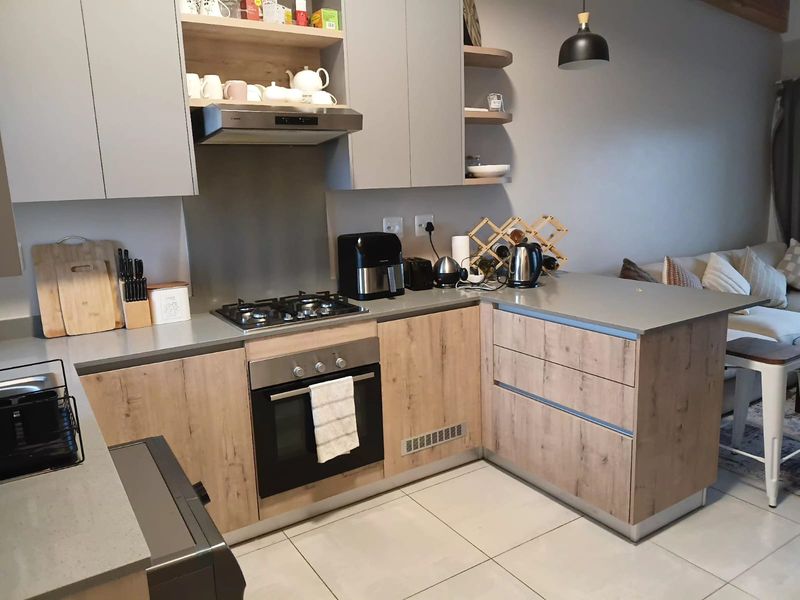 Modern open-plan kitchen featuring wood-grain cabinetry, stone countertops, integrated gas hob, and oven, seamlessly flowing into the adjacent living area.