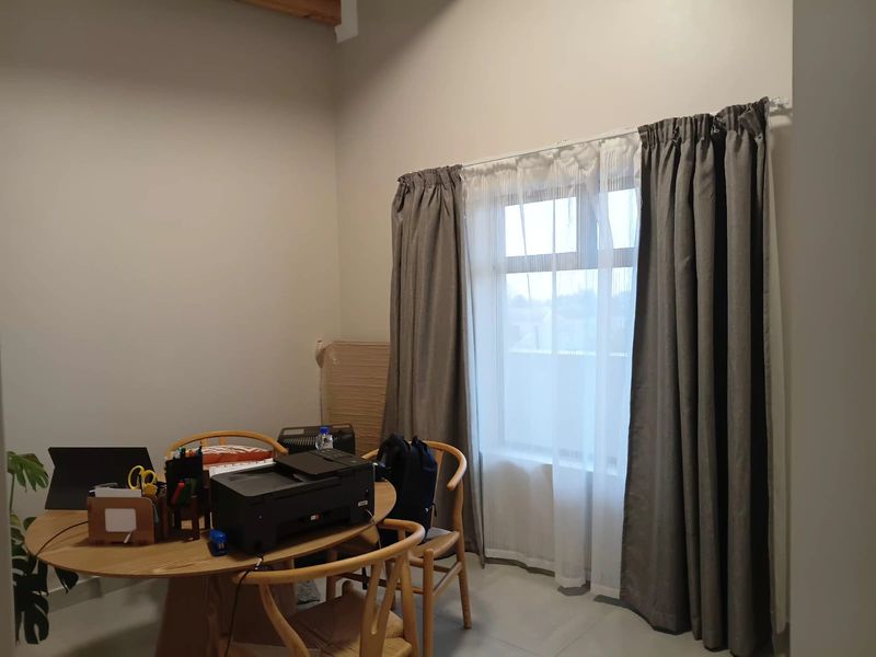 A functional office space featuring neutral walls, tiled flooring, and large windows with installed curtain tracks, providing a bright and versatile work environment.