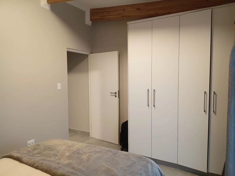 A well-maintained bedroom featuring built-in cupboards, neutral wall finishes, and an exposed timber ceiling beam.