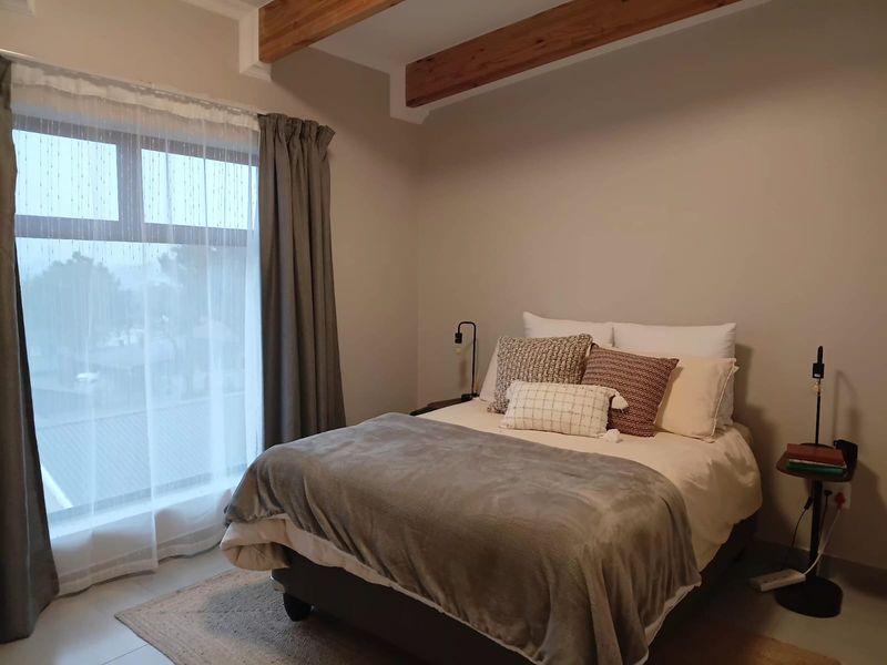 A well-maintained bedroom featuring exposed timber ceiling beams, neutral wall tones, and a large window providing natural light.