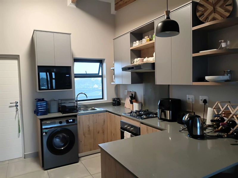 Modern kitchen featuring sleek grey and wood-tone cabinetry, stone countertops, integrated appliances, and a gas hob, offering a functional and contemporary cooking space.