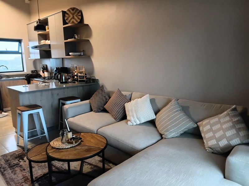 An open-plan living area featuring a modern kitchen with cabinetry, a breakfast island, and integrated shelving, seamlessly connected to the lounge space.