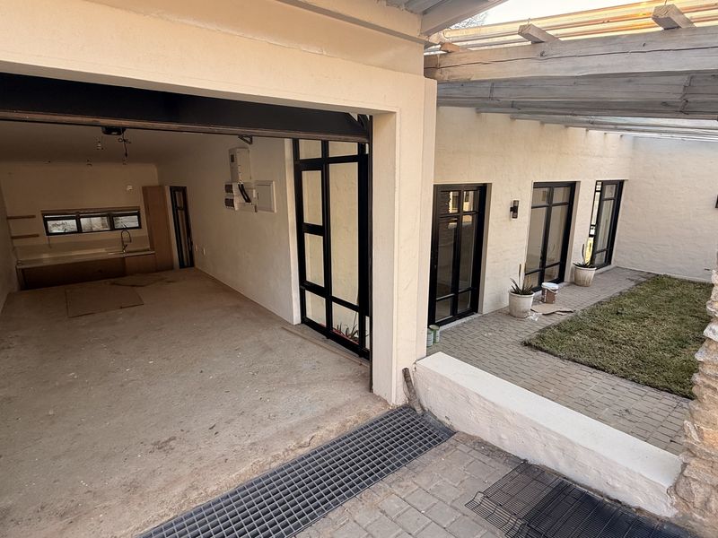 A versatile garage space featuring concrete flooring and direct access to a private paved courtyard with a timber pergola and stone feature wall.