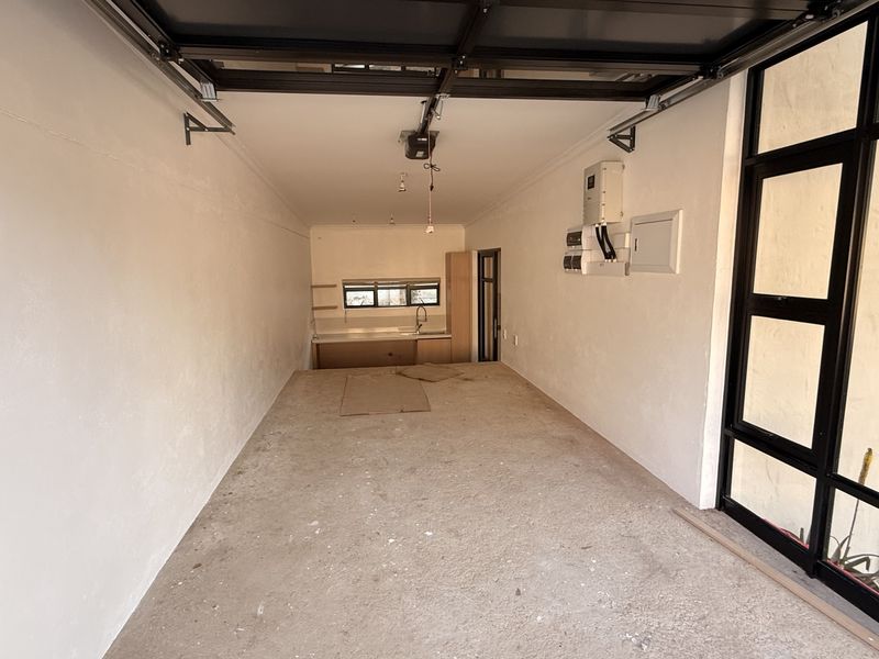 A spacious garage featuring a kitchenette area with sink, electrical distribution board, and large black-framed glass panels, offering potential for multi-purpose use.