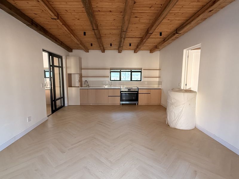 Modern open-plan kitchen and living area featuring herringbone timber flooring, exposed wooden ceiling beams, and sleek built-in cabinetry with a contemporary finish.