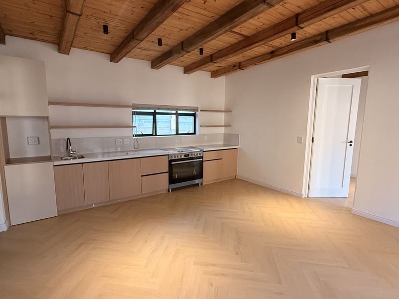 Modern kitchen featuring herringbone timber flooring, exposed wooden ceiling beams, sleek built-in cabinetry, and integrated stainless steel appliances in a bright, open space.