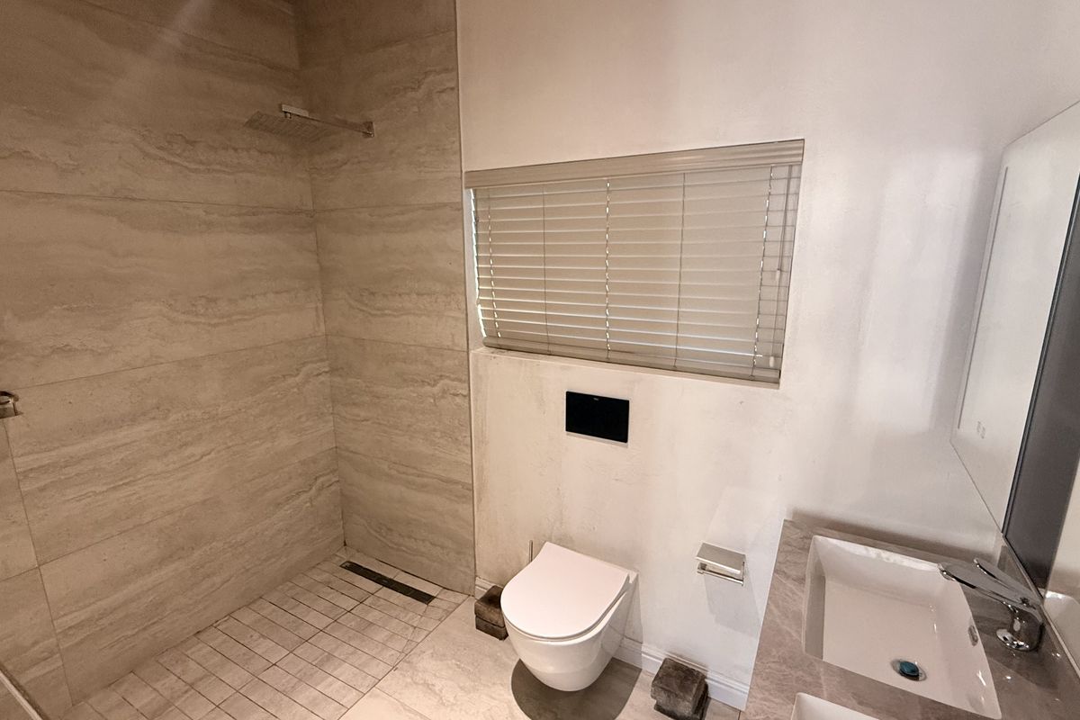 Modern bathroom featuring a walk-in shower with rain head, wall-mounted toilet, and a sleek vanity basin with contemporary finishes.
