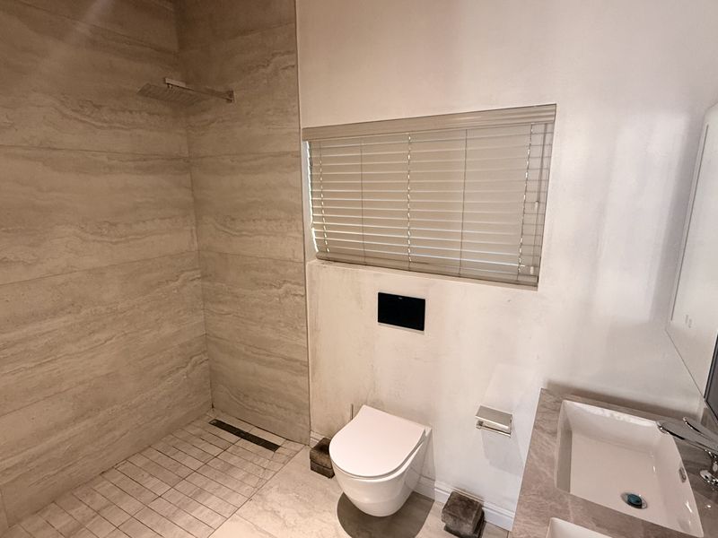 Modern bathroom featuring a walk-in shower with rain head, wall-mounted toilet, and a sleek vanity basin with contemporary finishes.