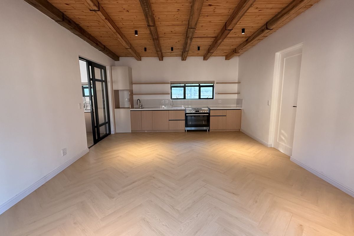 Modern open-plan living area featuring herringbone timber flooring, exposed beam ceiling, and a sleek kitchen with built-in cabinetry and integrated appliances.