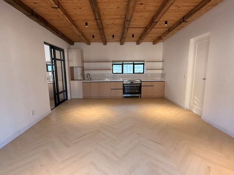 Modern open-plan living area featuring herringbone timber flooring, exposed beam ceiling, and a sleek kitchen with built-in cabinetry and integrated appliances.