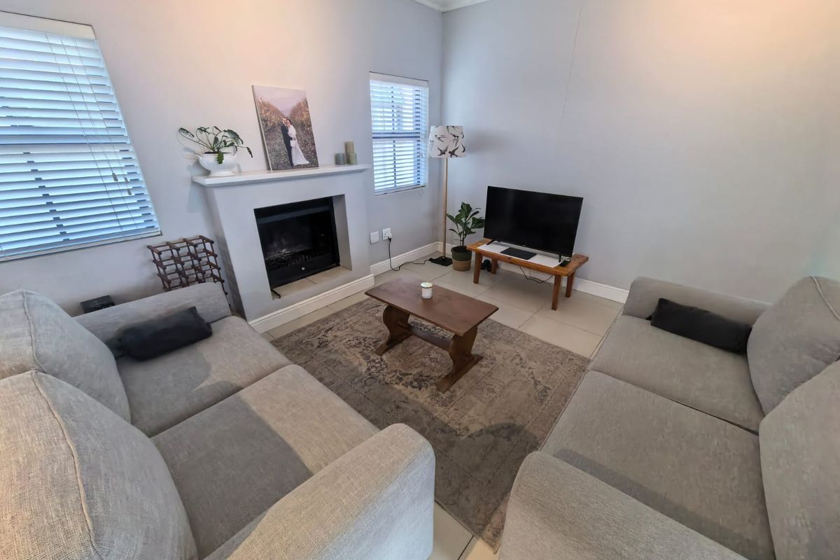 A cozy living room featuring a built-in fireplace, tiled flooring, and dual windows with venetian blinds, offering a comfortable and functional space.