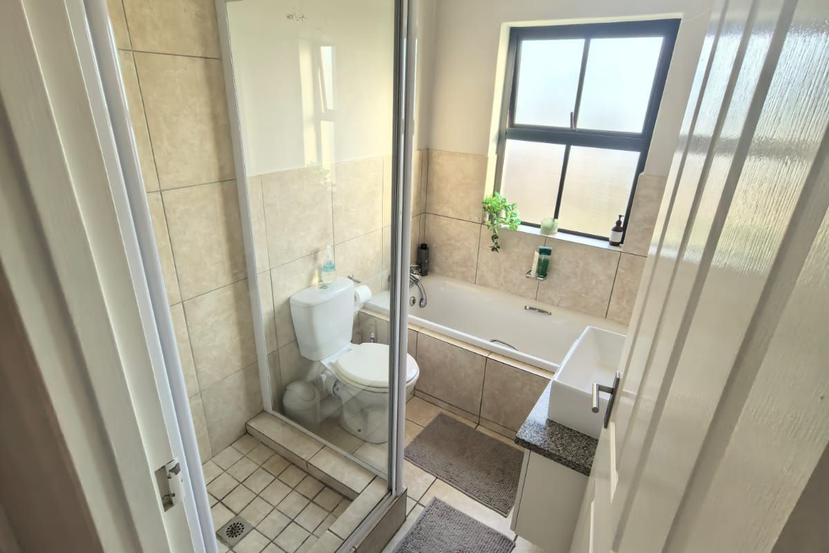 A functional bathroom featuring a glass-enclosed shower, a built-in bathtub, a vanity basin, and neutral floor-to-ceiling tiling.