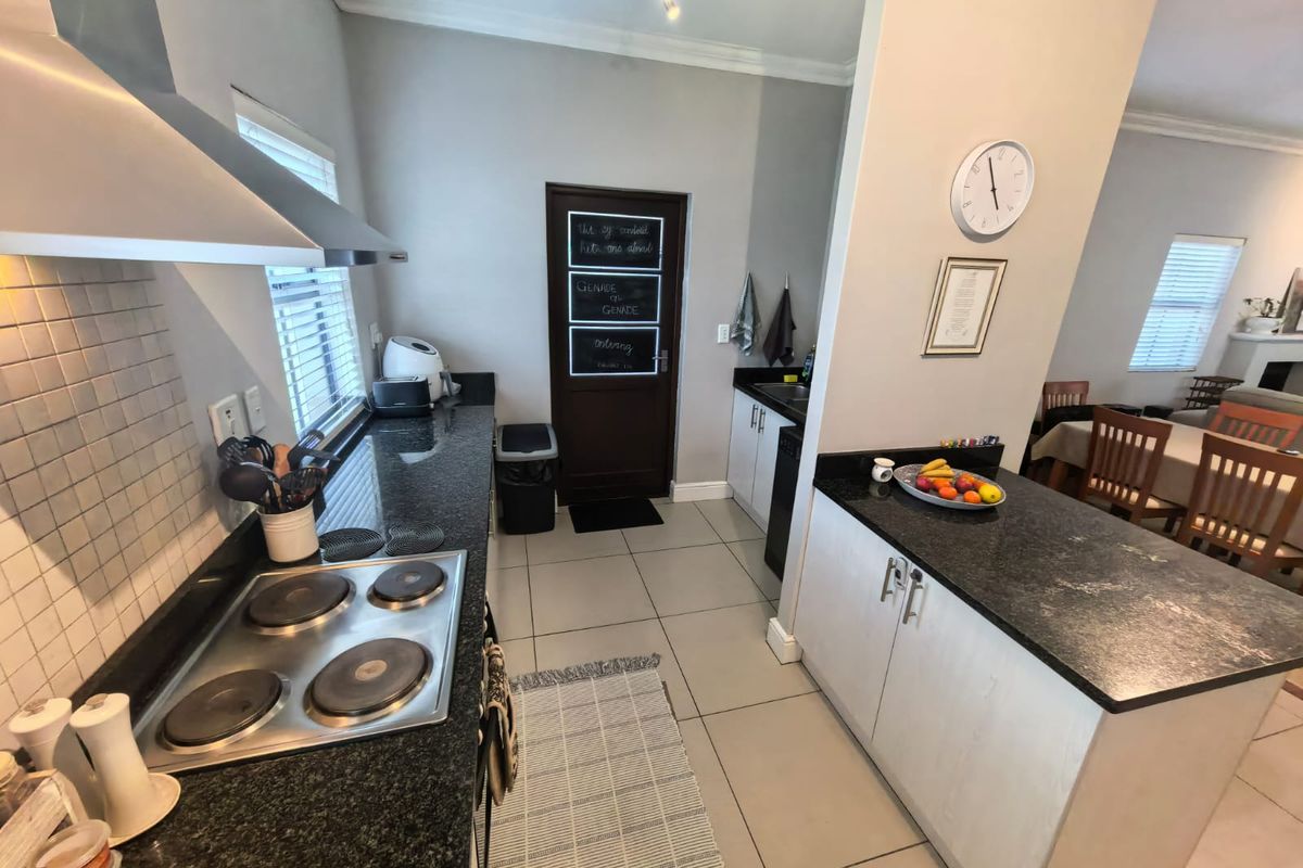 A functional kitchen featuring granite countertops, an electric hob with extractor fan, and ample built-in cabinetry, seamlessly flowing into the adjacent dining area.