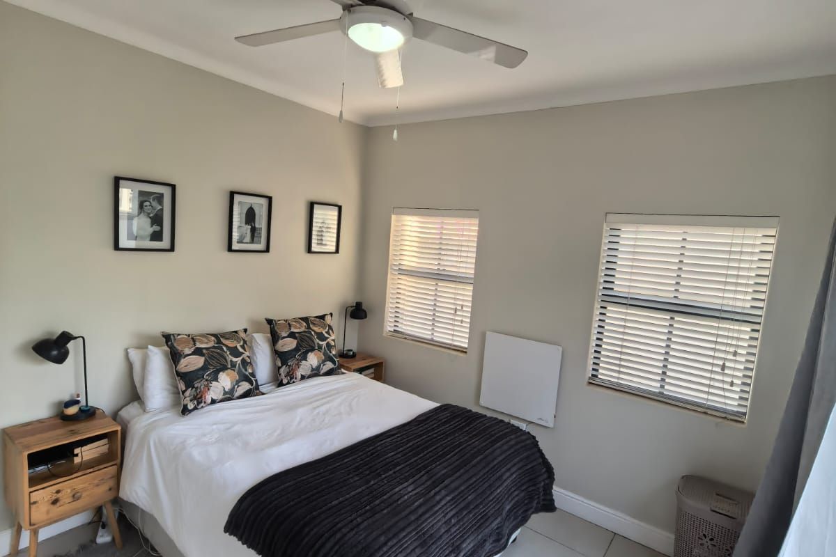 A well-maintained bedroom featuring neutral wall tones, tiled flooring, a ceiling fan, and dual windows fitted with venetian blinds.
