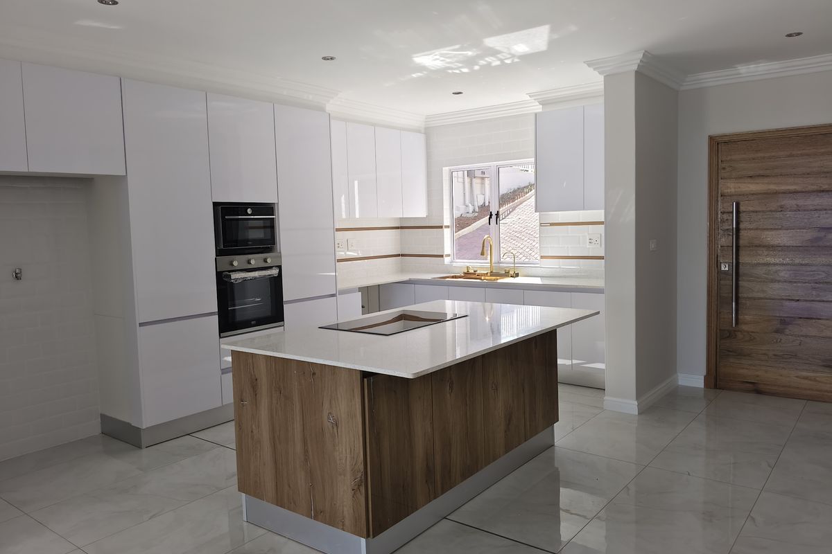 Modern kitchen featuring white glossy cabinetry, a central island with stone countertops, built-in oven and microwave, and elegant brass fixtures.