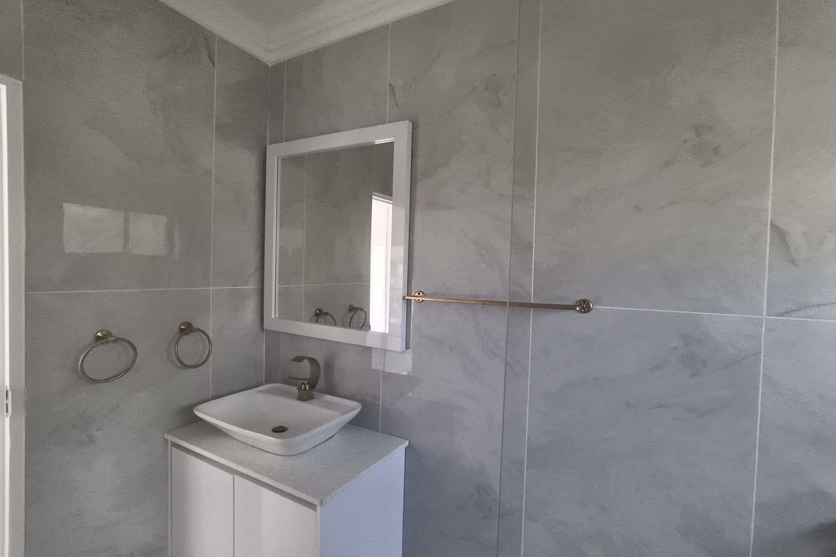Modern bathroom featuring grey wall tiles, a white vanity cabinet with a vessel sink, and contemporary fixtures.