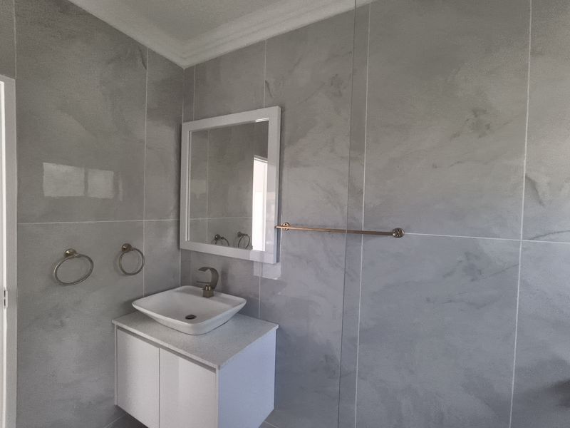 Modern bathroom featuring grey wall tiles, a white vanity cabinet with a vessel sink, and contemporary fixtures.