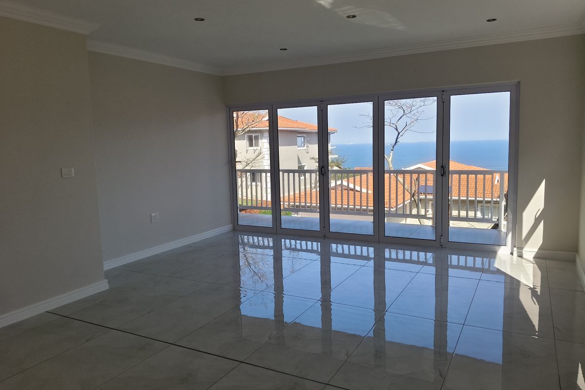 A bright, empty living room featuring polished tiled floors, recessed lighting, and large folding glass doors that open to a scenic ocean view.