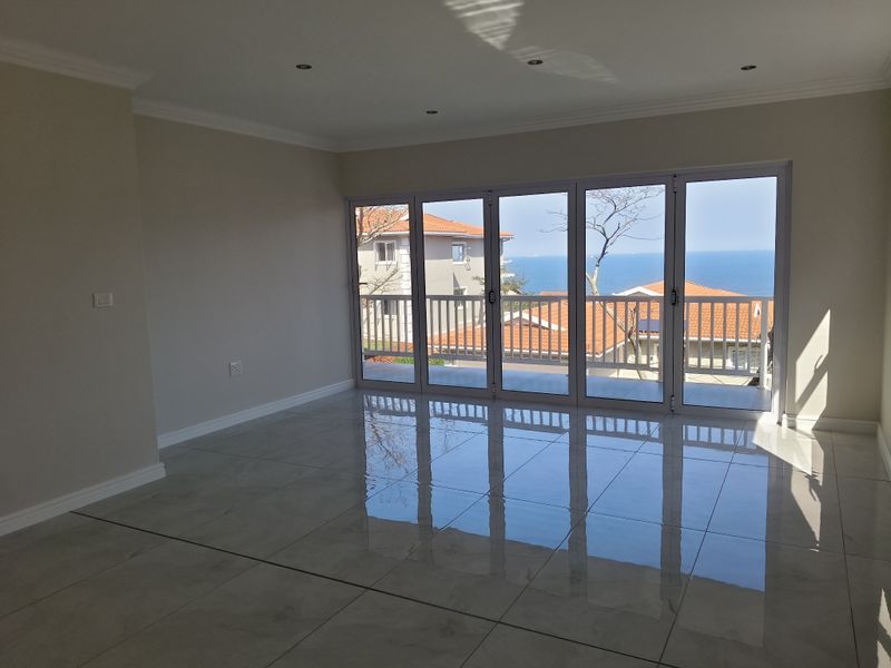 A bright, empty living room featuring polished tiled floors, recessed lighting, and large folding glass doors that open to a scenic ocean view.