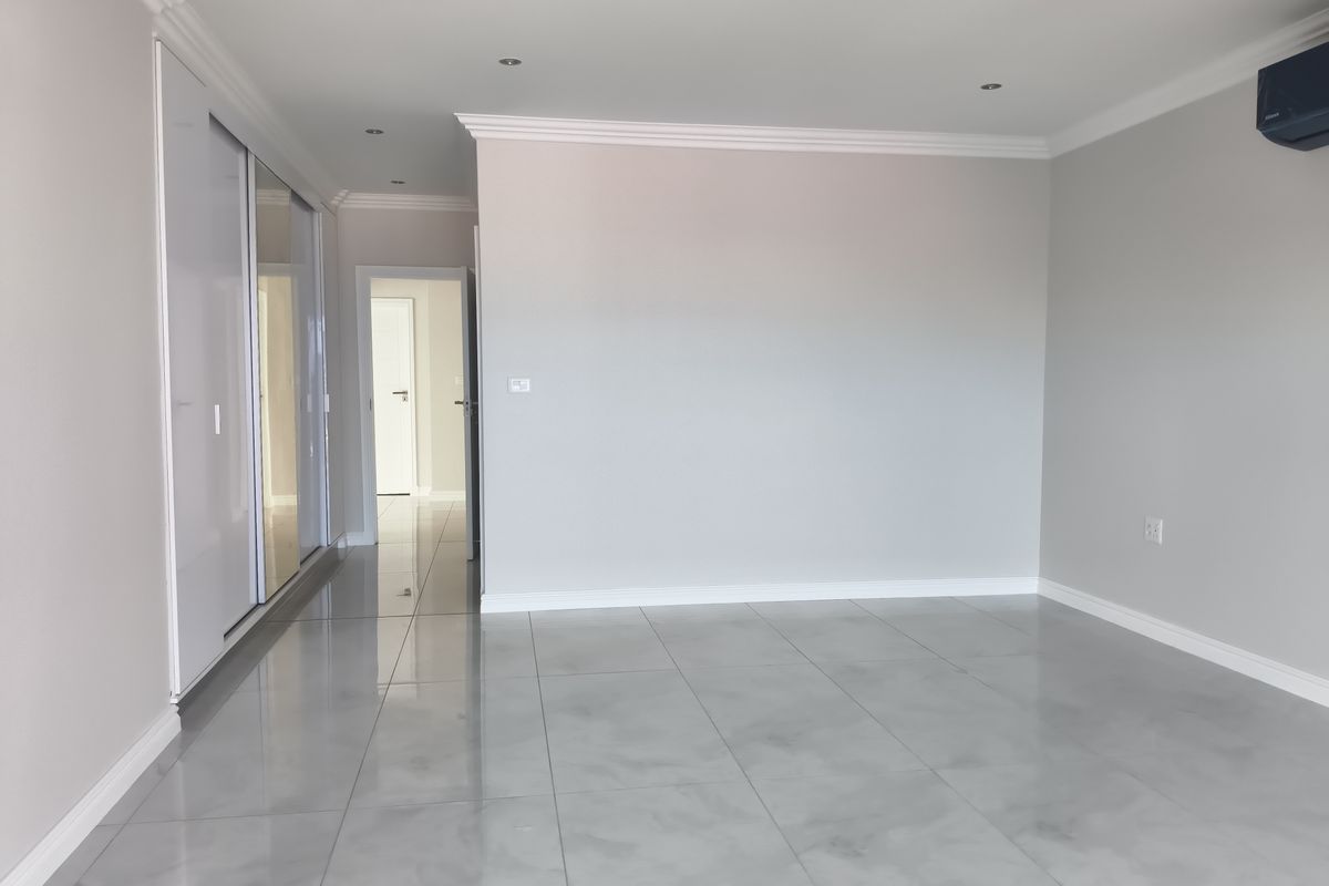 A spacious, modern bedroom featuring polished porcelain floor tiles, built-in cupboards with sliding mirror doors, recessed lighting, and a wall-mounted air conditioning unit.