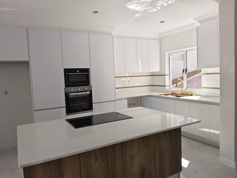 Modern kitchen featuring a central island with induction hob, quartz countertops, glossy white cabinetry, built-in oven and microwave, and elegant gold fixtures.
