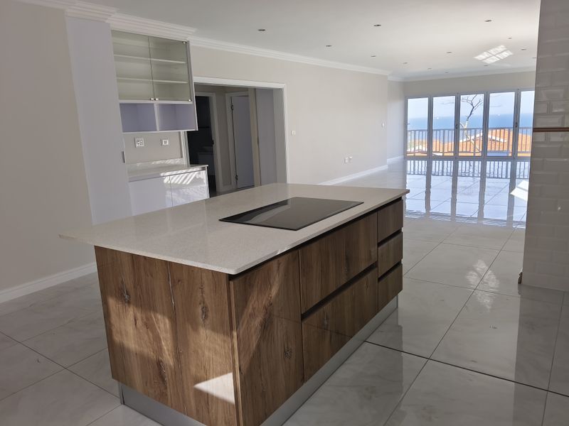 Spacious open-plan kitchen and living area featuring a modern island with induction cooktop, sleek cabinetry, and large sliding doors opening to a balcony with views.