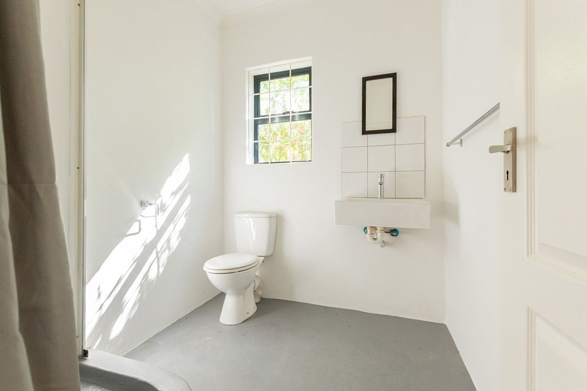 A simple, functional bathroom featuring a wall-mounted basin, toilet, and tiled splashback, finished with neutral walls and grey flooring.