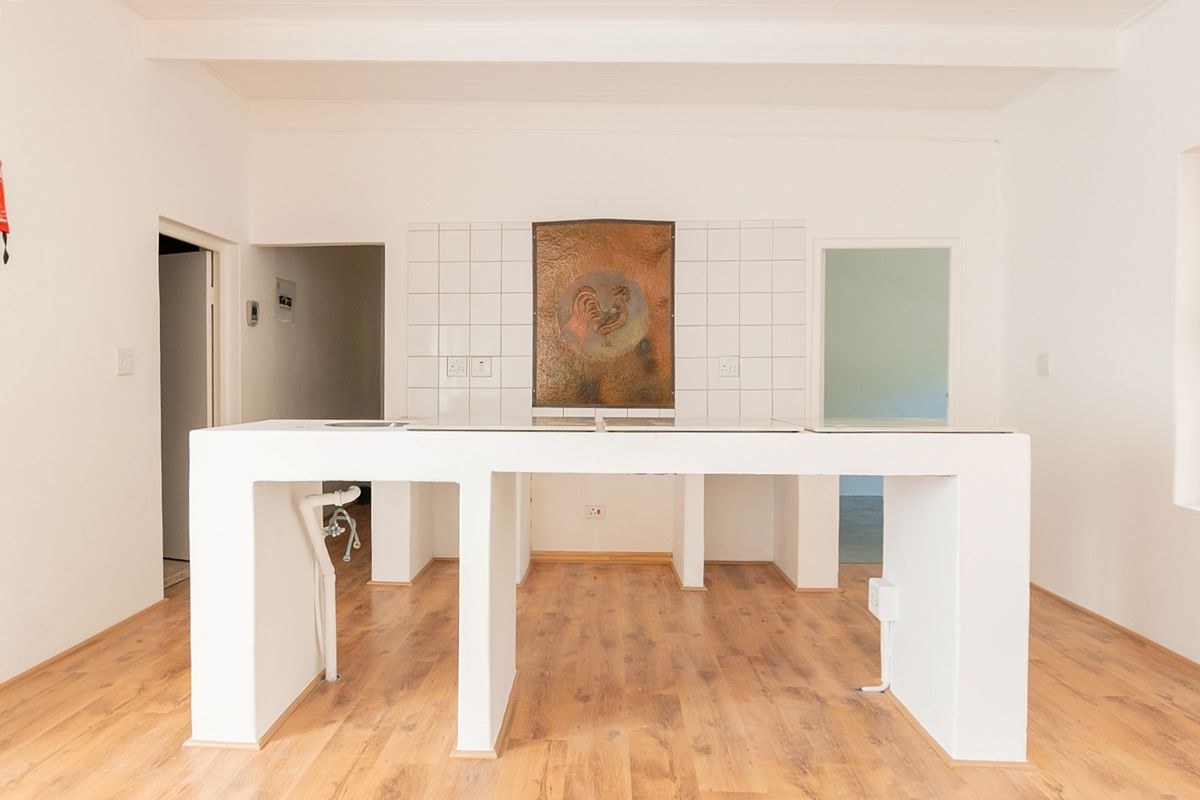 An empty kitchen space featuring a built-in island with tiled splashback and laminate flooring, offering a blank canvas for renovation.