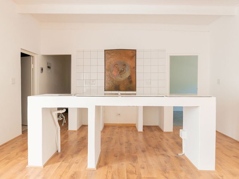 An empty kitchen space featuring a built-in island with tiled splashback and laminate flooring, offering a blank canvas for renovation.