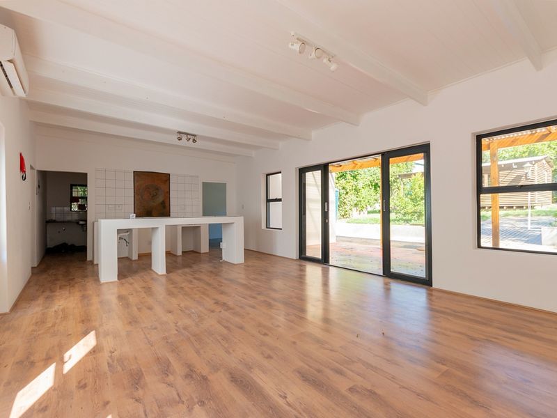 Spacious open-plan living area featuring laminate flooring, exposed beam ceilings, and sliding glass doors leading to an outdoor patio.