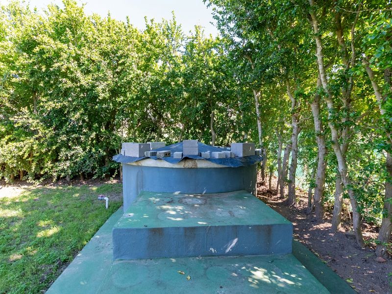 A garden area featuring a large water tank on a concrete base, surrounded by mature trees and dense foliage.