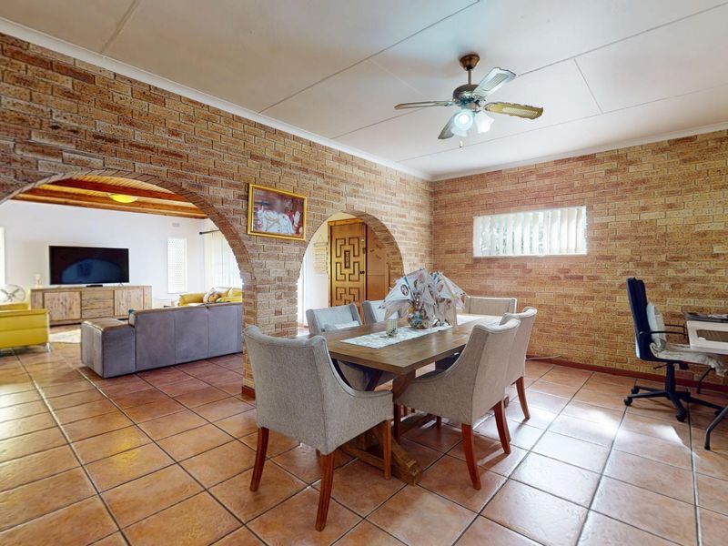 Open plan dining and living area featuring exposed brick walls, distinctive brick archways, tiled flooring, and a ceiling fan.