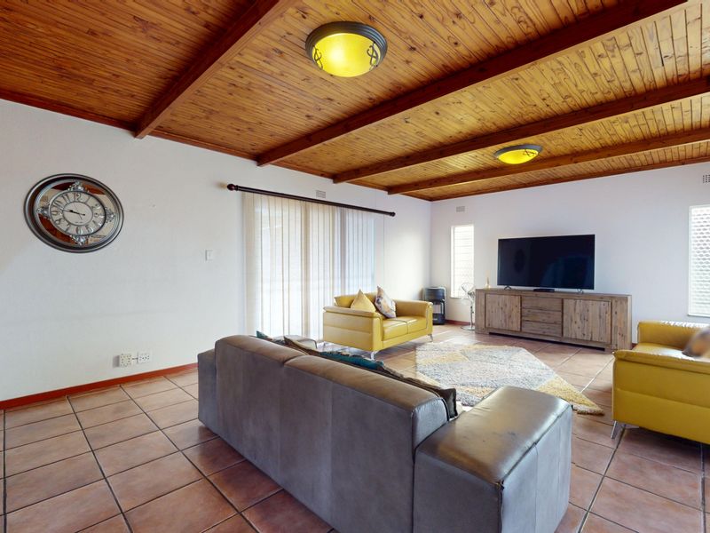 Spacious living room featuring a warm exposed timber beam ceiling, terracotta-style tiled flooring, and a brick feature wall with access to the outdoors.