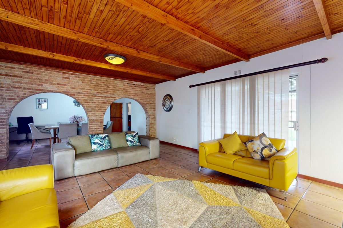 Spacious living room featuring a warm timber beam ceiling, exposed brick feature wall with arched openings, and tiled flooring with access to the outdoors.