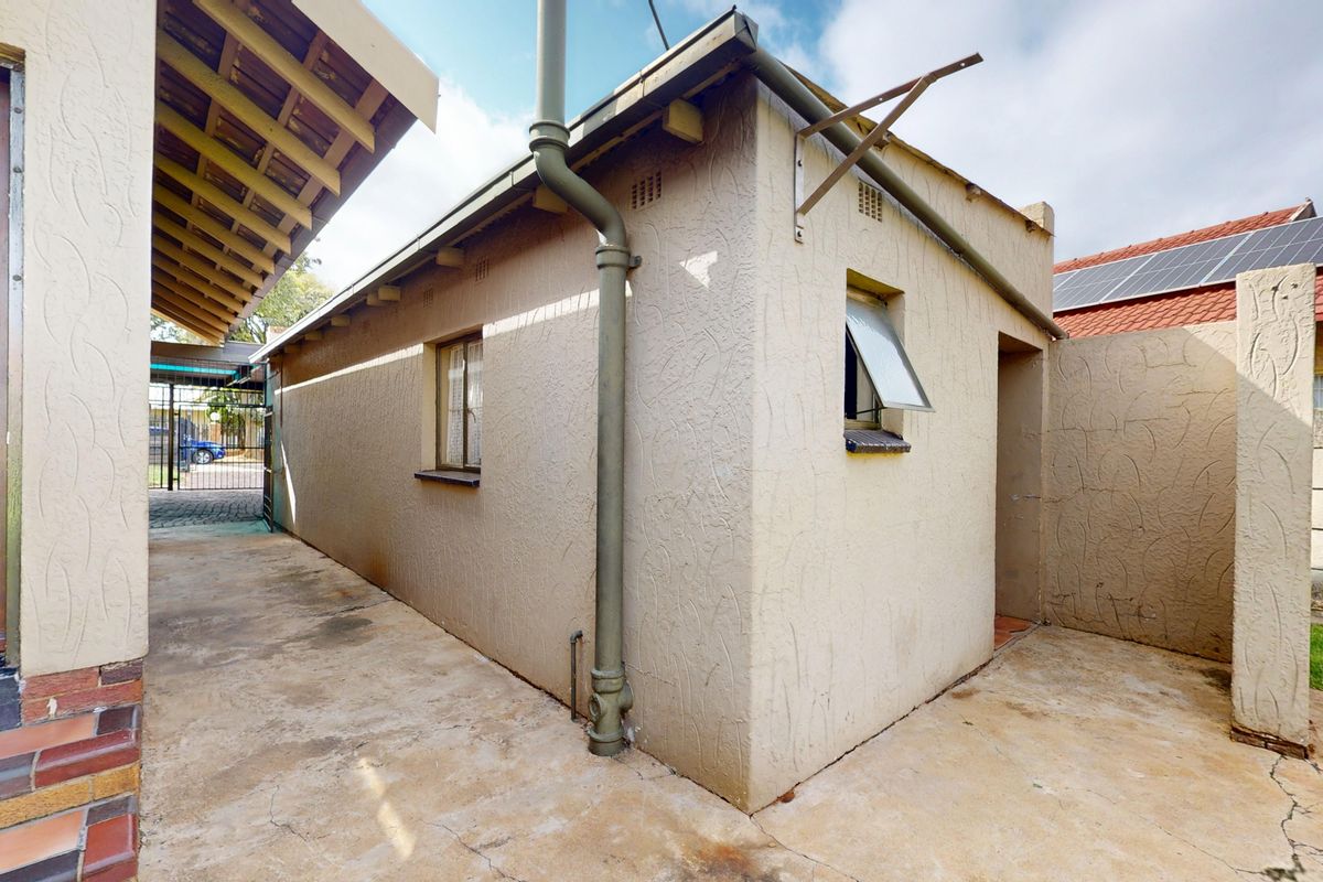 Rear exterior view of the property featuring concrete paving, a downpipe, and access to the side yard area.