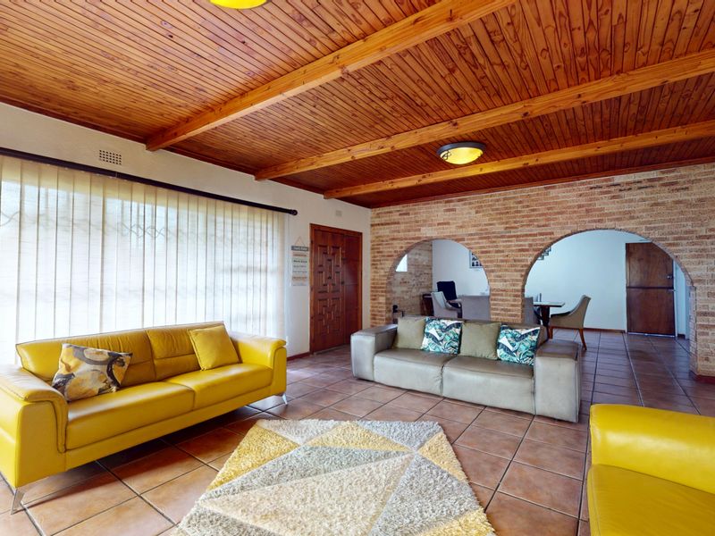 Spacious living room featuring a warm timber-clad ceiling, exposed brick feature wall with decorative archways, and durable tiled flooring.