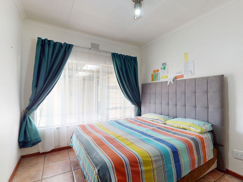 A functional bedroom featuring tiled flooring, a central light fixture, and a window with curtains, providing a comfortable and well-lit living space.