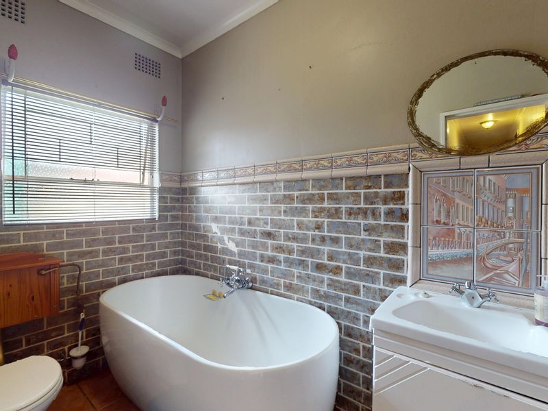 A dated bathroom featuring a freestanding bathtub, wall-mounted toilet, and vanity basin, finished with decorative brick-style wall tiles and a painted upper wall section.