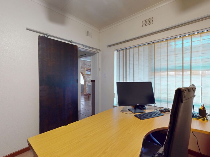 A functional home office space featuring a sliding barn door and large window with vertical blinds, providing natural light and access to adjacent rooms.