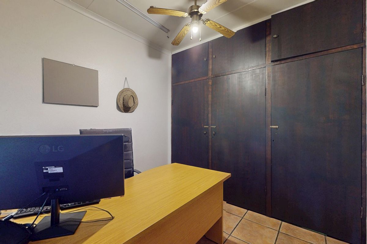 A bedroom featuring dark wood built-in cupboards, a ceiling fan, and tiled flooring, currently utilized as a home office space.