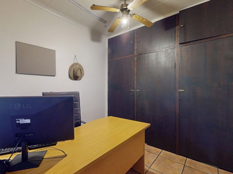 A bedroom featuring dark wood built-in cupboards, a ceiling fan, and tiled flooring, currently utilized as a home office space.