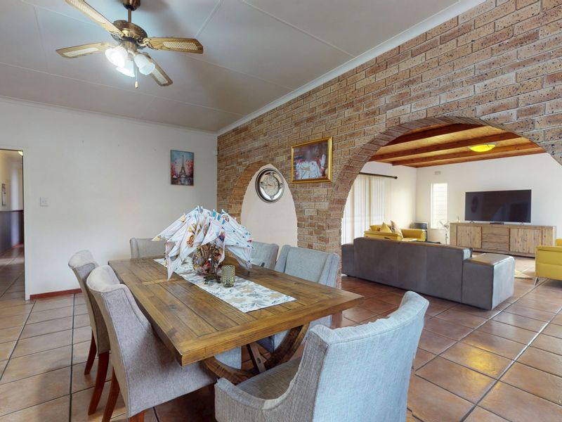 Open plan dining and living area featuring distinctive exposed brick archways, tiled flooring, and exposed timber ceiling beams in the adjacent living space.