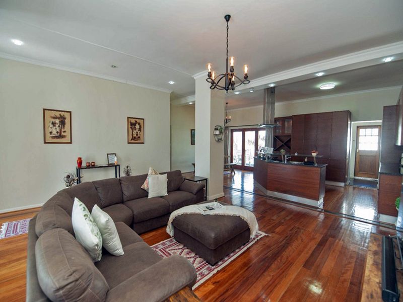 Spacious open-plan living area featuring rich hardwood flooring, a modern kitchen with island, and seamless flow to the outdoor space through french doors.
