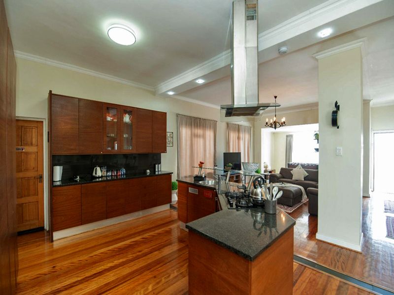 Open-plan kitchen and living area featuring rich wooden cabinetry, granite countertops, a gas hob with extractor, and polished hardwood flooring throughout.
