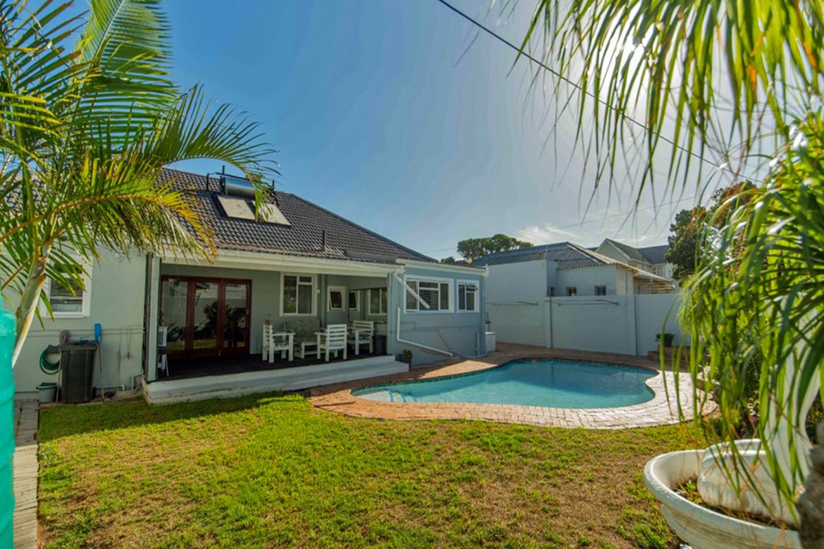 Rear exterior view of the guest house featuring a swimming pool, covered patio area, and a private garden with boundary walls.